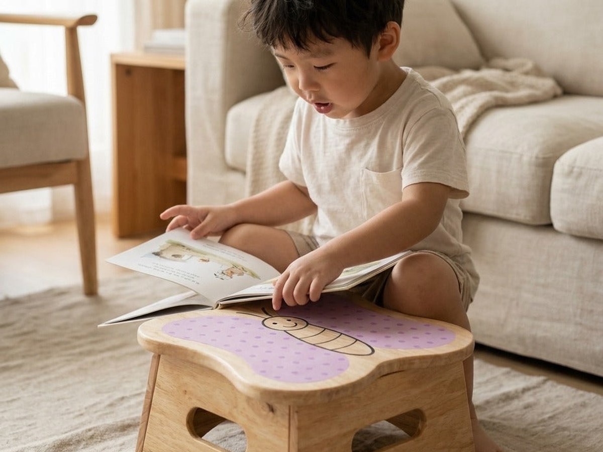 A young child on the floor reading a picture book aloud, the book open on the lilac butterfly top of a Stobbi